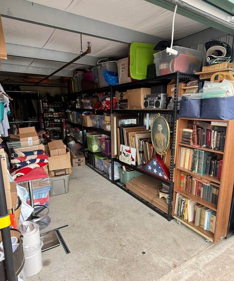 The unit's main aisle today: shelving stacked with bins, framed art and portraits, antique books, sneakers, and a folded American flag
